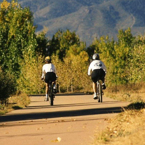 Two people ride bicycles on a scenic trail