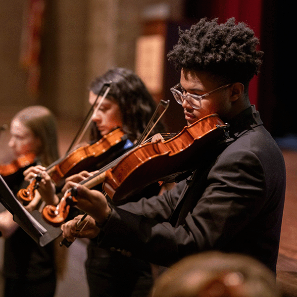 Three violinists perform in an orchestra